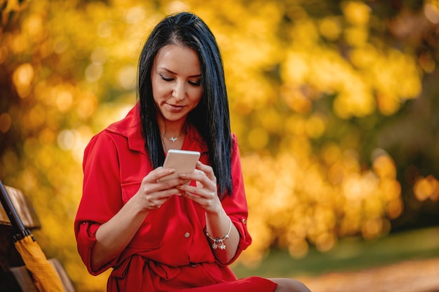 Mulher jovem feliz lendo mensagem no smartphone na natureza do outono.