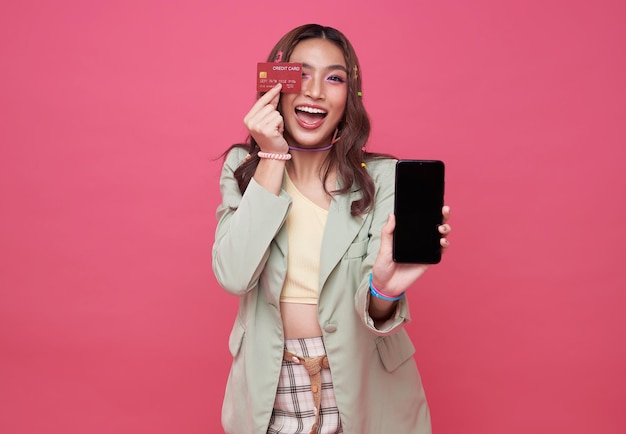 Mulher jovem feliz mostrando cartão de crédito e telefone celular sobre fundo rosa