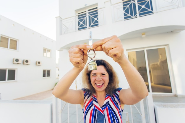 Mulher jovem feliz na frente da nova casa com as novas chaves da casa