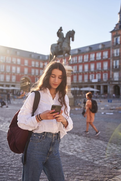 Mulher jovem feliz olhando para smartphone perto do Monumento Equestre ao Rei Filipe III de Espanha na Plaza Mayor de Madrid