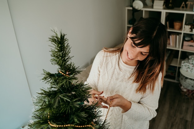 Mulher jovem feliz preparando a casa para a época do Natal. Decoração de árvore com lindas bolas de Natal.