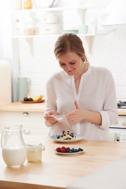 Mulher jovem feliz preparando lanches saborosos na mesa da cozinha à luz da manhã