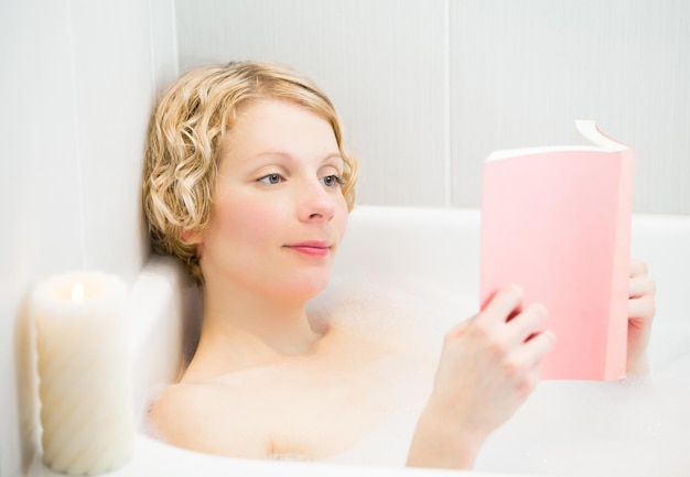 Mulher jovem feliz relaxando e lendo um livro no banho