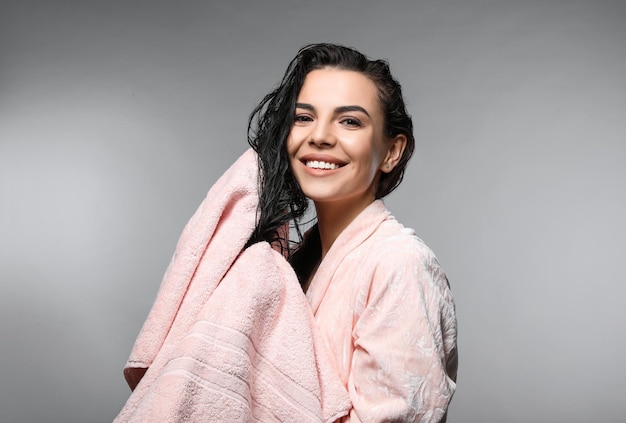 Mulher jovem feliz secando o cabelo com toalha depois de lavar em fundo cinza claro