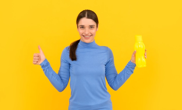 Mulher jovem feliz segura garrafa esportiva com água com o polegar para cima gesto de saúde