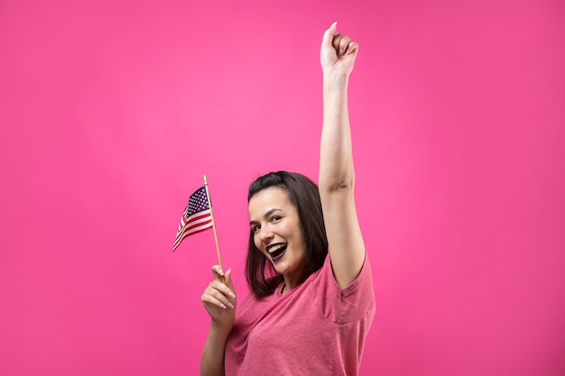 Mulher jovem feliz segurando a bandeira americana contra um fundo rosa estúdio