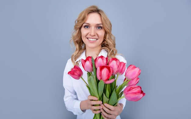 Mulher jovem feliz segurando flores de tulipa da primavera em fundo cinza