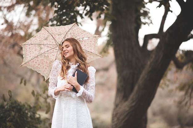 Mulher jovem feliz segurando um livro de papel e um guarda-chuva pequeno vintage