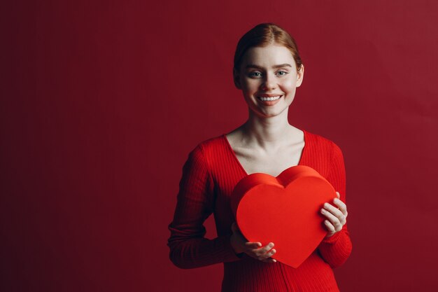 Mulher jovem feliz segurando uma caixa em forma de coração no dia dos namorados em fundo vermelho