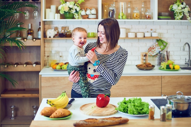Mulher jovem feliz, segurando uma criança de 1 ano e cozinhar juntos na cozinha
