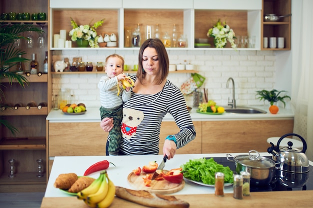 Mulher jovem feliz, segurando uma criança de 1 ano e cozinhar juntos na cozinha