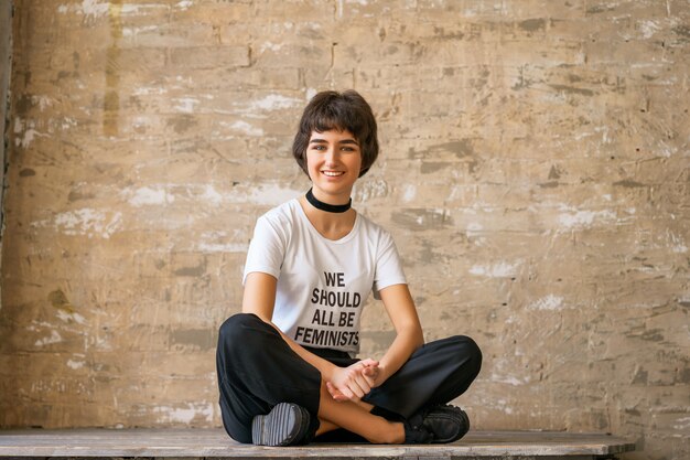 Mulher jovem feliz senta-se em uma camiseta branca com as palavras que todos devemos ser feministas, conceito