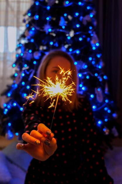 Foto mulher jovem feliz sentada com um copo de champanhe e luz de bengala ao lado do natal