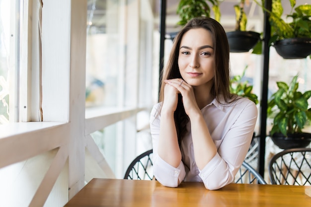 Mulher jovem feliz sentada e esperando o pedido no café