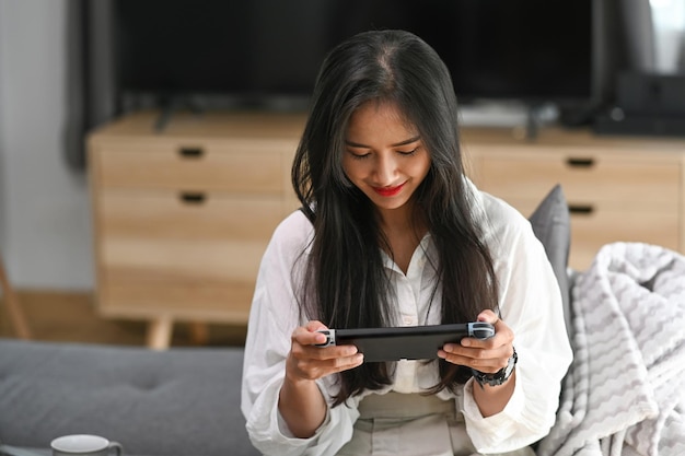 Mulher jovem feliz sentada no sofá e jogando videogame