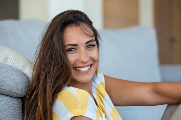 Mulher jovem feliz sentada no sofá em casa e olhando para a câmera Retrato de uma linda mulher sorrindo e relaxando durante o verão