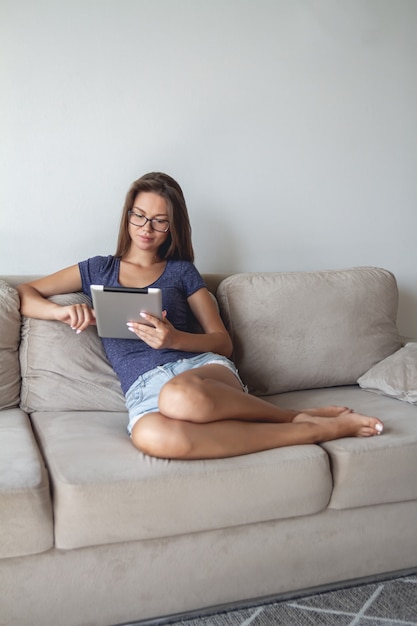 Mulher jovem feliz sentado no sofá e usando o tablet em casa.