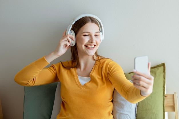 Mulher jovem feliz usando fones de ouvido e usando smartphone em casa