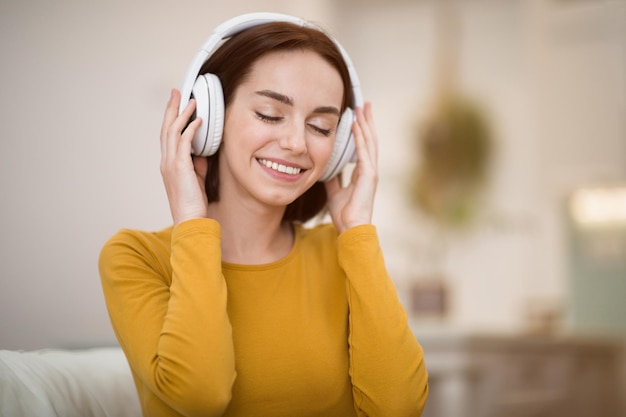 Mulher jovem feliz usando fones de ouvido sem fio em casa