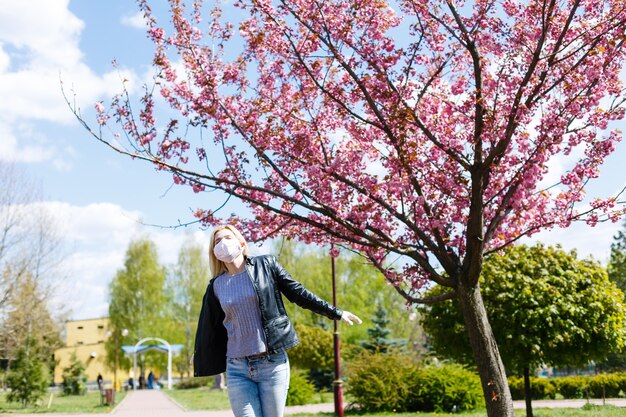 Mulher jovem feliz usando máscara facial para proteção contra vírus em pé ao ar livre em um dia ensolarado de primavera.