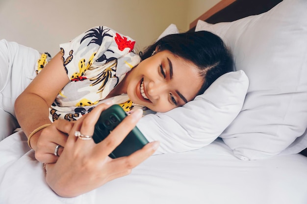 Mulher jovem feliz verificando seu telefone enquanto estava deitada na cama