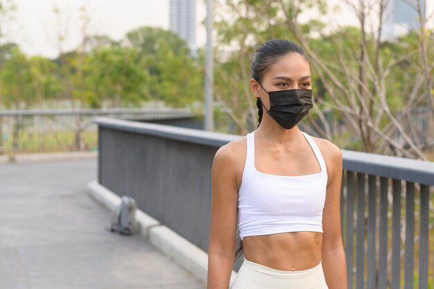 Mulher jovem fitness em roupas esportivas usando máscara facial enquanto se exercita na cidade