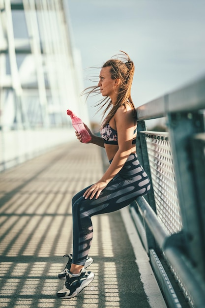 Mulher jovem fitness está descansando após treinamento duro na ponte do rio e água potável.