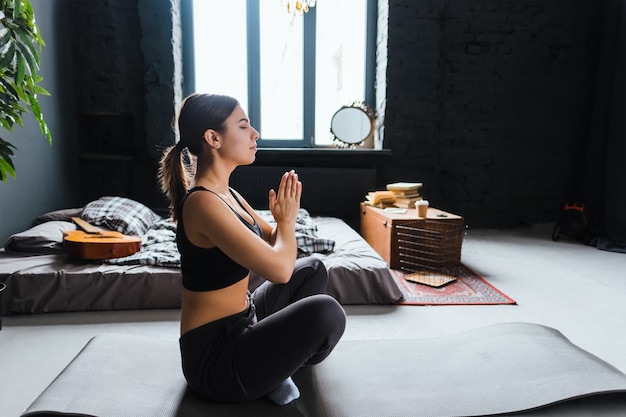 Mulher jovem fitness meditando, fazendo ioga dentro de casa em casa perto da cama