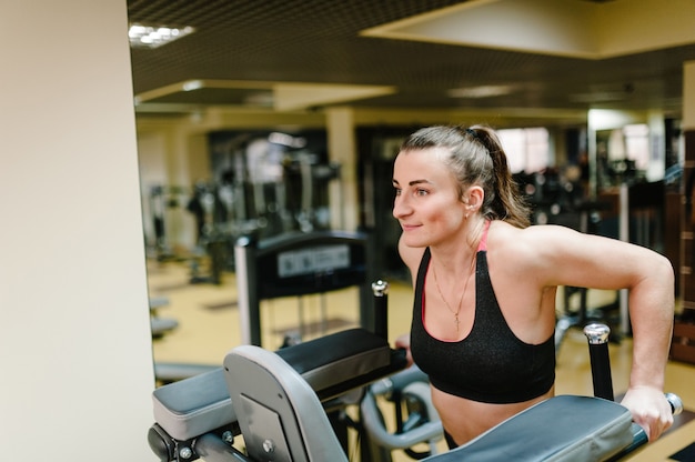 Mulher jovem fitness pendurada e trabalhando com a pressão dos músculos abdominais na barra horizontal no clube de ginástica