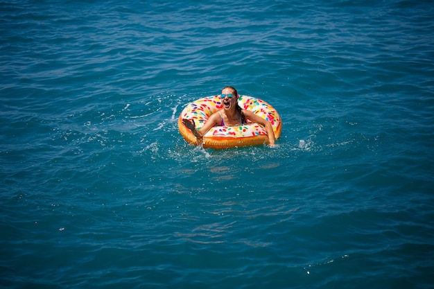 Mulher jovem flutuando em uma rosquinha grande inflável no mar azul-turquesa transparente. vista de uma senhora esbelta relaxante de férias na turquia, egito, mar mediterrâneo.