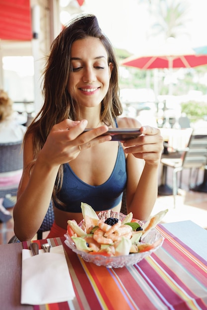Foto mulher jovem fotografando comida com telefone na mesa em um restaurante