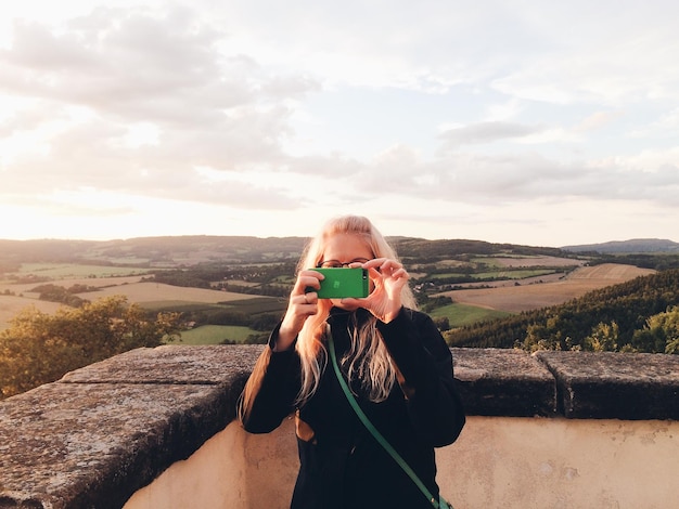 Foto mulher jovem fotografando no celular contra o céu