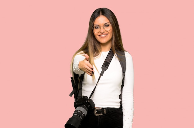 Mulher jovem fotógrafo apertando as mãos para fechar um bom negócio no fundo rosa isolado