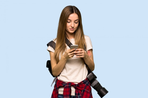 Mulher jovem fotógrafo enviando uma mensagem com o celular na parede azul isolada