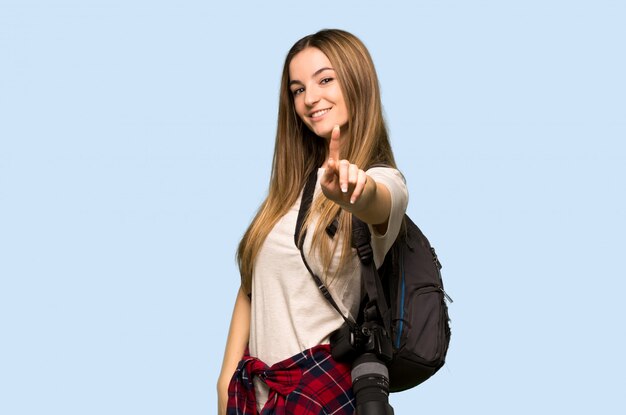 Mulher jovem fotógrafo mostrando e levantando um dedo na parede azul isolada