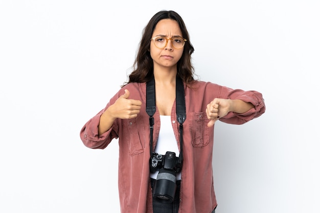 Mulher jovem fotógrafo sobre fundo branco isolado, fazendo sinais de bom-ruim. indeciso entre sim ou não