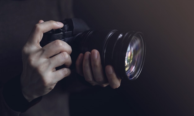 Foto mulher jovem fotógrafo usando a câmera para tirar foto. tom escuro. foco seletivo na mão
