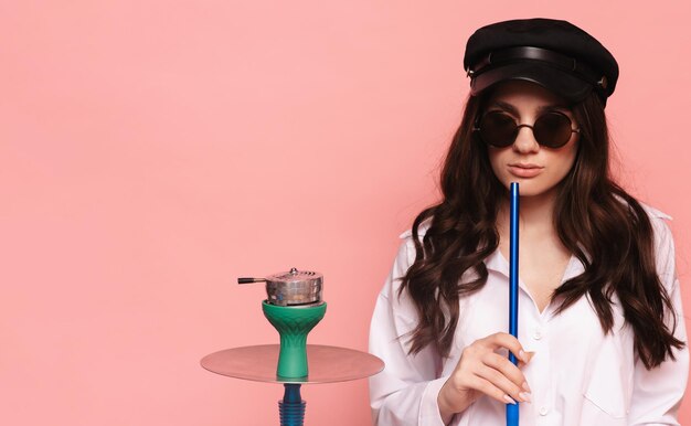 Mulher jovem fuma cachimbo de água, shisha em um fundo rosa. lugar para o seu texto.