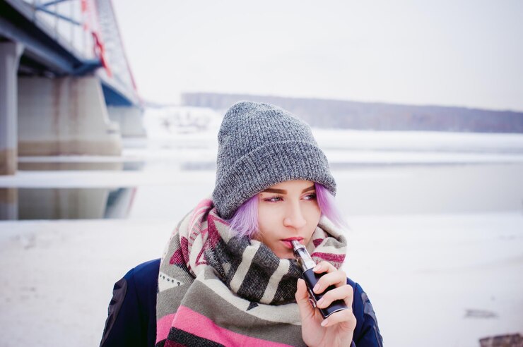 Foto mulher jovem fumando enquanto estava de pé junto à ponte contra o céu durante o inverno