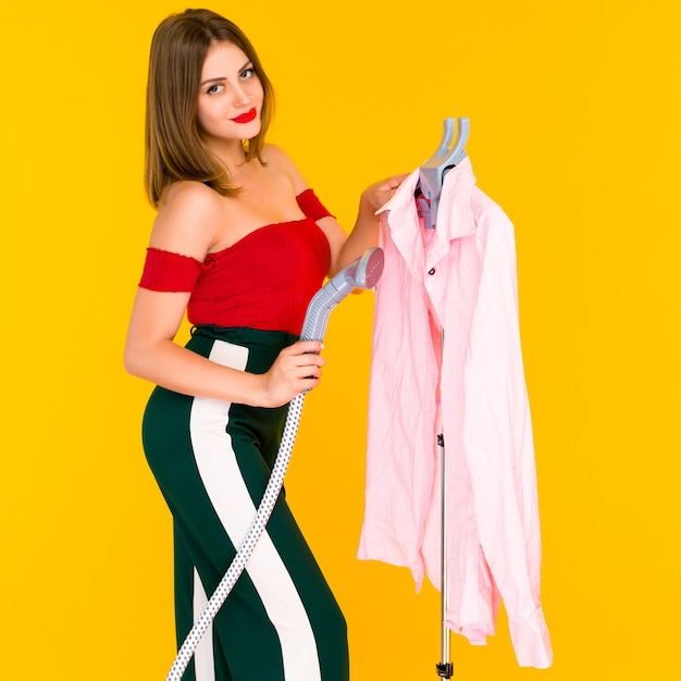 Foto mulher jovem fumegando camisa rosa na lavanderia em amarelo