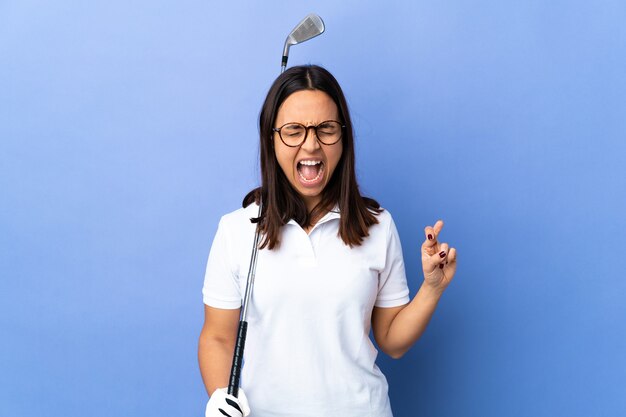 Mulher jovem golfista em uma parede colorida isolada cruzando os dedos