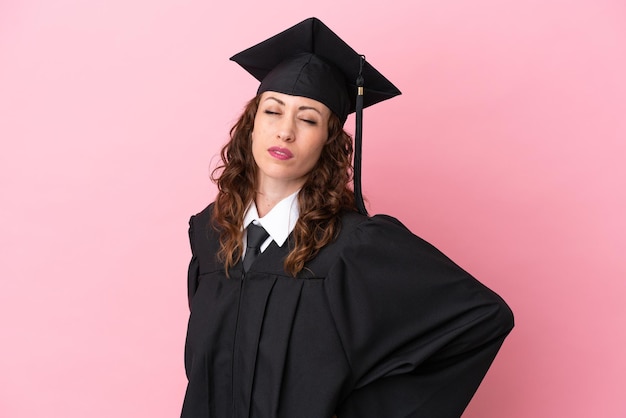 Mulher jovem graduada da universidade isolada em fundo rosa, sofrendo de dor nas costas por ter feito um esforço