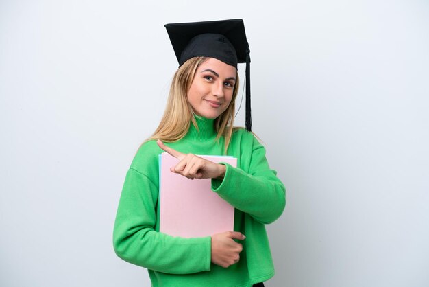 Mulher jovem graduada da universidade isolada no fundo branco apontando para o lado para apresentar um produto