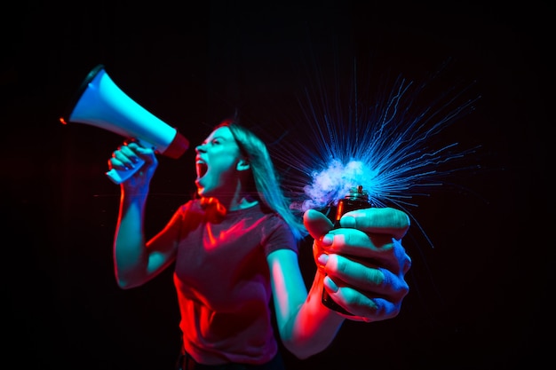 Mulher jovem gritando com um megafone e fumando uma luz de néon em um fundo preto