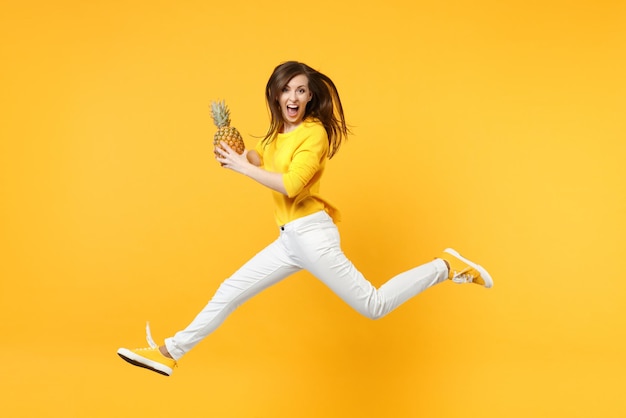 Mulher jovem gritando em roupas casuais pulando segure fruta fresca de abacaxi maduro isolada no fundo da parede laranja amarela no estúdio. Estilo de vida vívido de pessoas, relaxe o conceito de férias. Espaço de cópia de mock up