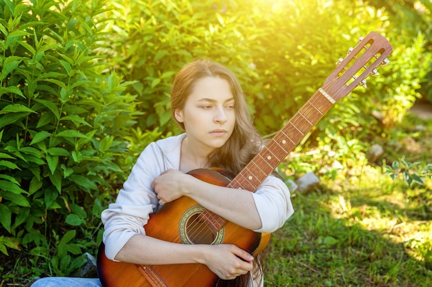 Mulher jovem hippie sentada na grama tocando guitarra no parque ou jardim