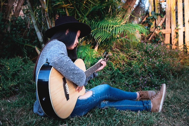 Mulher jovem hippie tocando uma guitarra no jardim