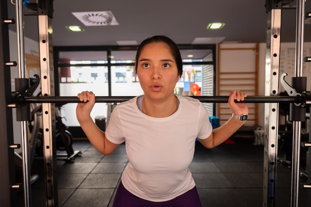 Foto mulher jovem hispânica de esportes levantando pesos no ginásio