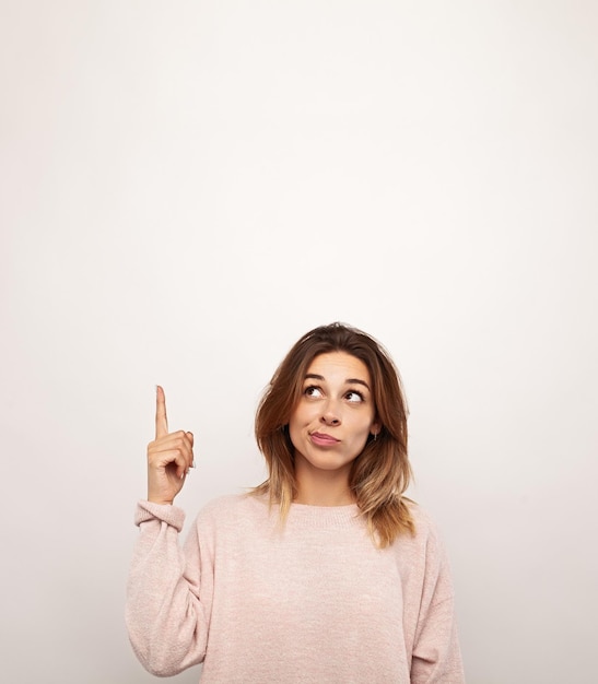 Foto mulher jovem insegura apontando contra um fundo branco