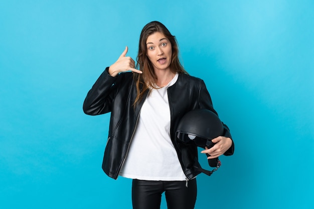 Mulher jovem Irlanda segurando um capacete de motocicleta isolado no fundo azul, fazendo gesto de telefone. Ligue-me de volta sinal